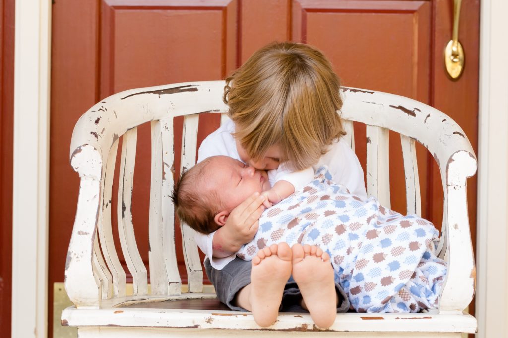 big brother holding a newborn baby on a bench