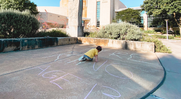 A kid writes with chalk on a sidewalk.