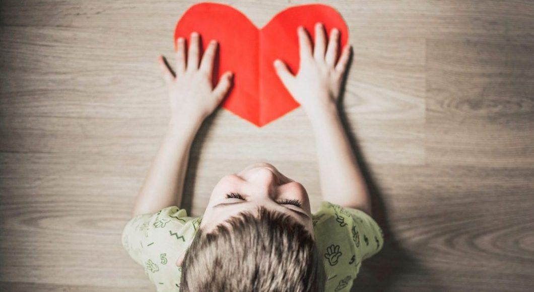A boy has his hands on top of a paper heart cut-out.