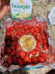 Boursin cheese with tomatos and seasoning in a pan lined with aluminum foil