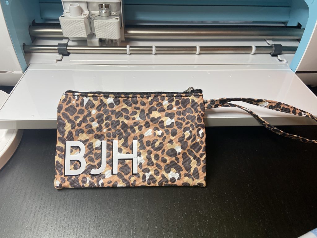 A leopard print wrist wallet, monogrammed in white, bold caps with black shadowing for depth