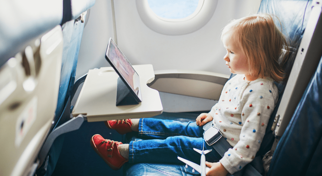 A little girl sits on an airplane watching a tablet.