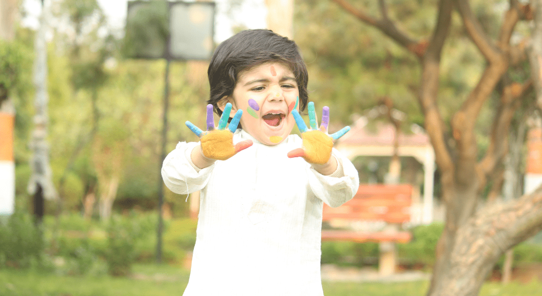Little boy dressed in white with color powder on his hands and face