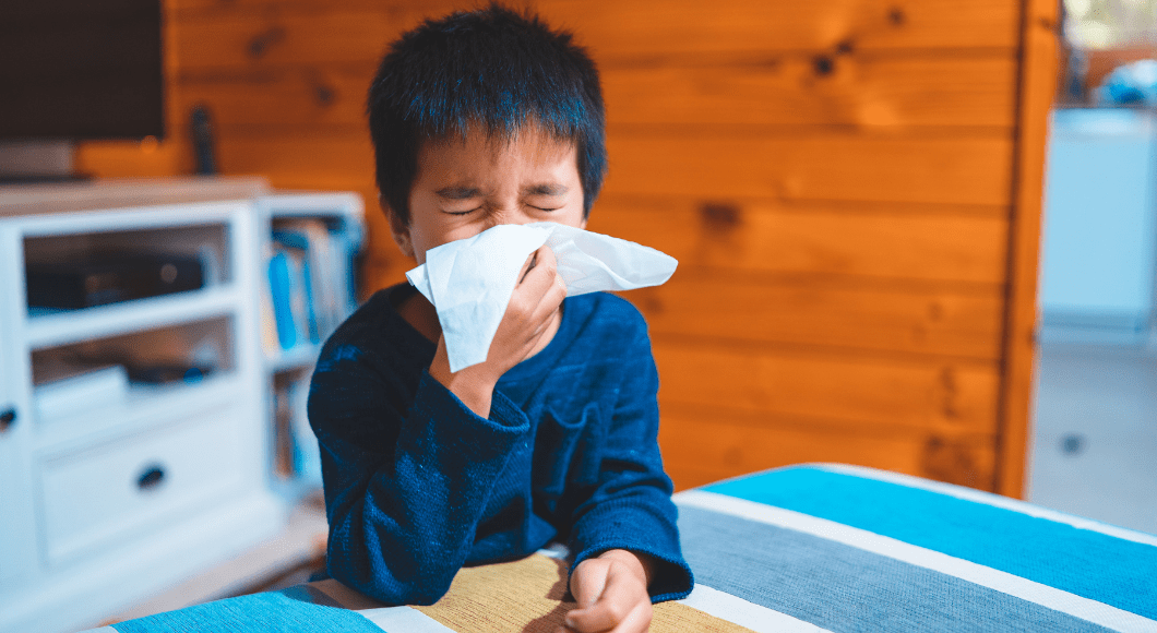 A boy blows his nose into a tissue.