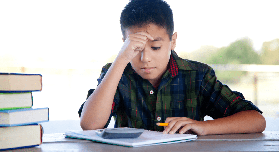 A kid struggles with math homework and look at a piece of paper and a calculator.