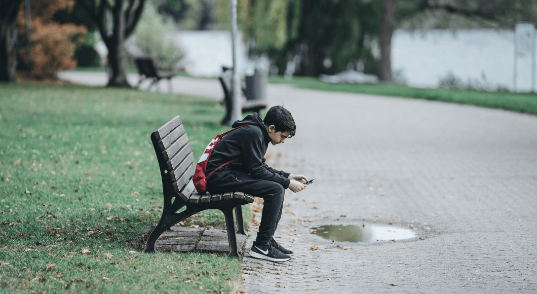 A teenage boy sits on a bench looking at his phone.