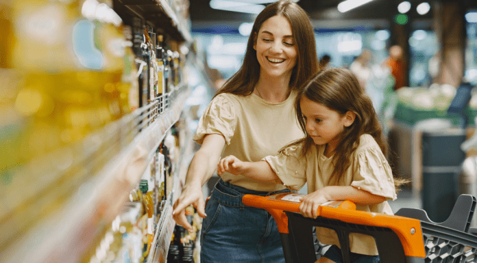 A mom points out grocery store prices to her daughter who sits in a cart.