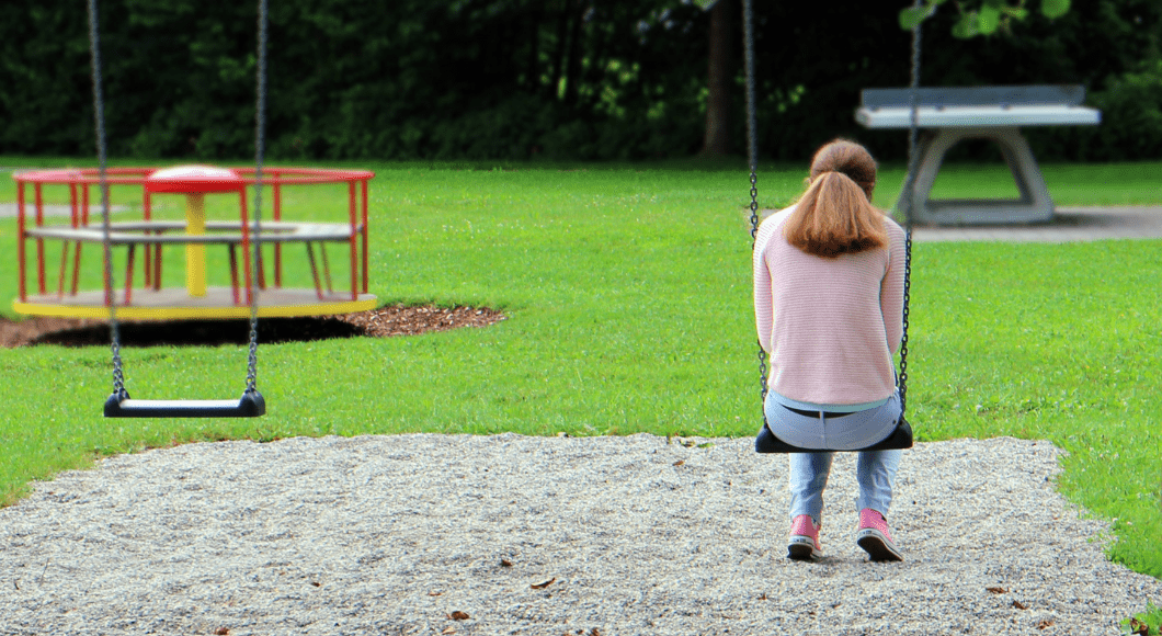 A mom sits alone on a swing at a playground.