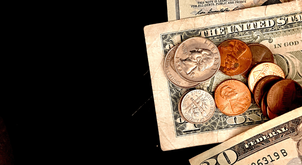Cash and coins laid out on the right side of the image over a black background. 