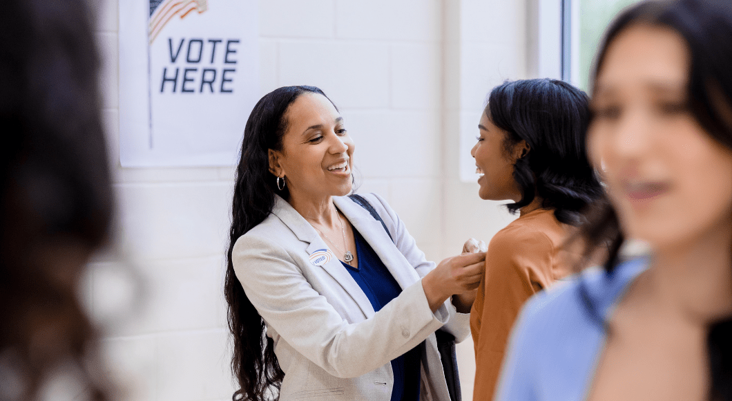 A woman places a I Voted sticker on another woman.