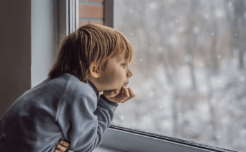 A young boy looks out the window to winter weather.