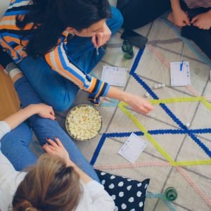 A family sits on the floor and plays dice, an inside activity, while snacking on a bowl of popcorn.