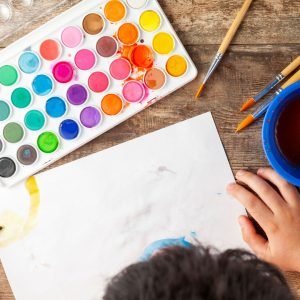 A child paints a picture with watercolors on a piece of paper--a great inside activity.