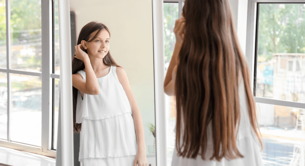 Young girl with very long hair looks at her reflection in the mirror.