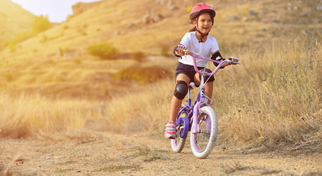 A girl wears a helmet, elbow pads, and knee pads while mountain biking.