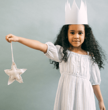 Little girl holds a wand and wears a princess crown and gown.