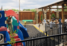 Kids play on a playground adjacent to a restaurant's outdoor patio where the grownups sit, eat, and watch the kids.