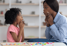 A speech pathologist models vowel sounds to a little girl who mimics her mouth shape.