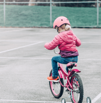 Little girl learns to ride a bike on a tennis court.