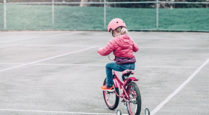 Little girl learns to ride a bike on a tennis court.